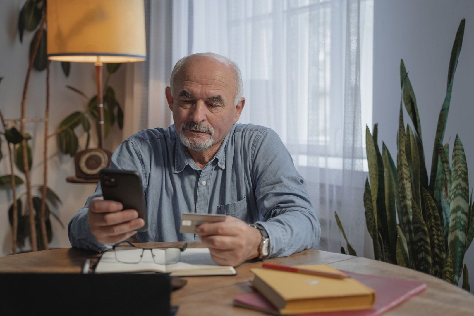 Äldre man håller en smartphone och ett betalkort vid ett bord