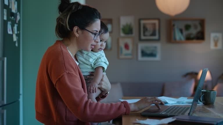 Förälder arbetar vid laptop med barn i famnen hemma
